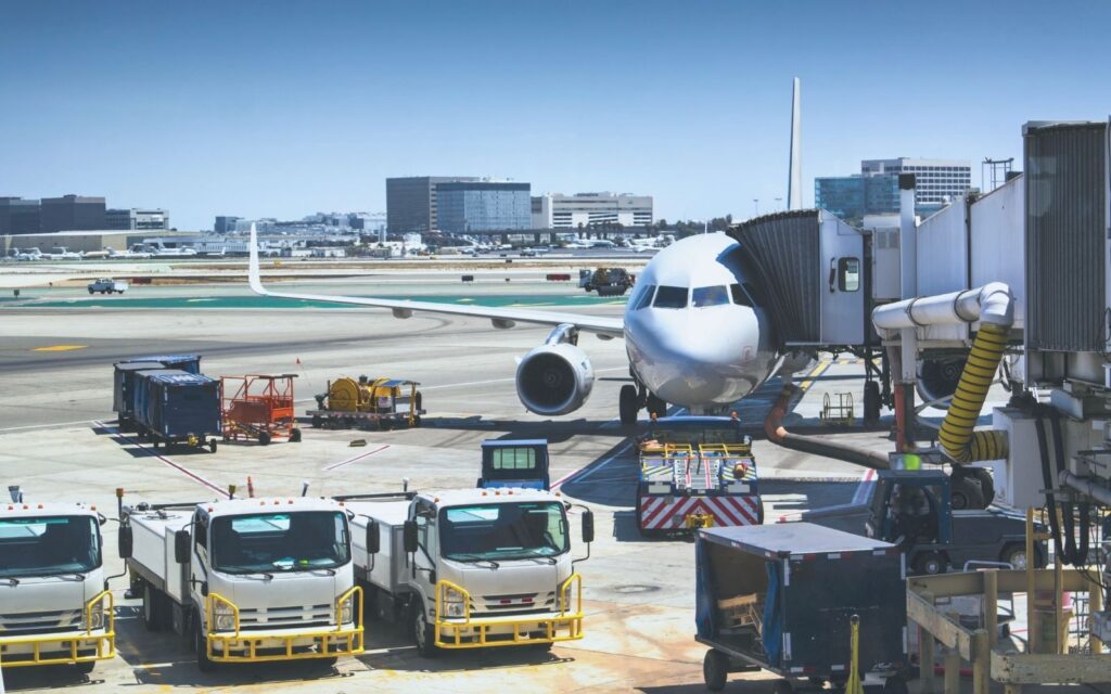 Ground service trucks and baggage containers beside a passenger aircraft at a terminal gate.