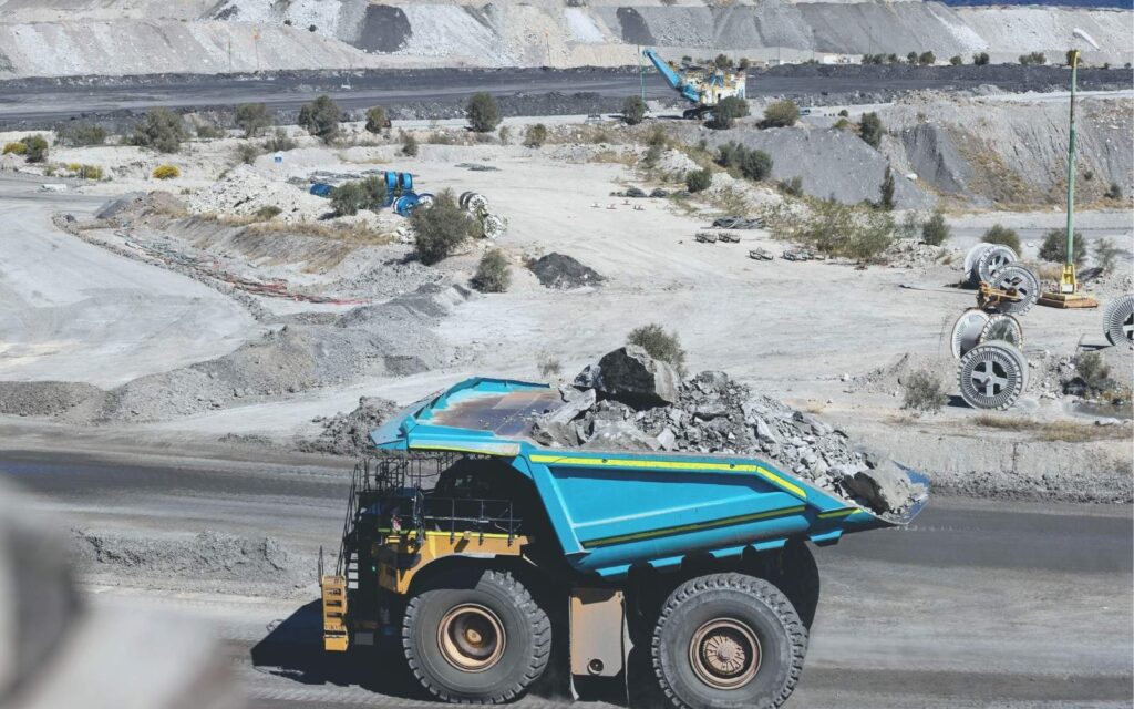 Blue and yellow haul truck carrying rocks through a quarry.