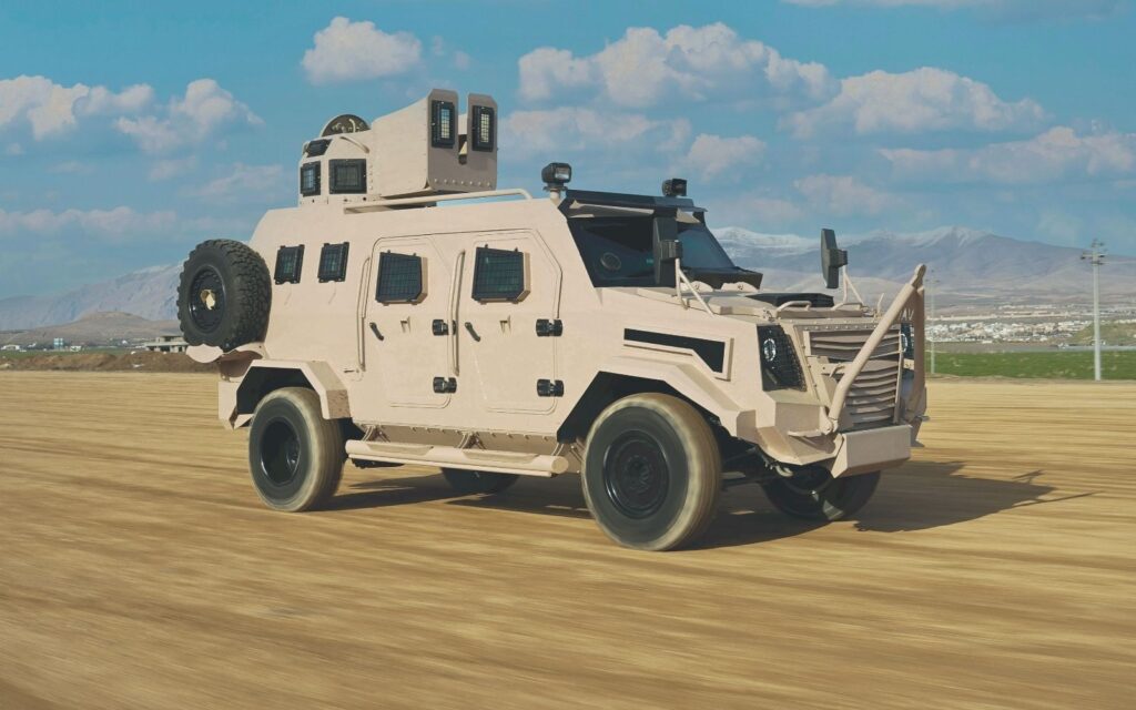 Tan armored military vehicle driving across dry grassland.